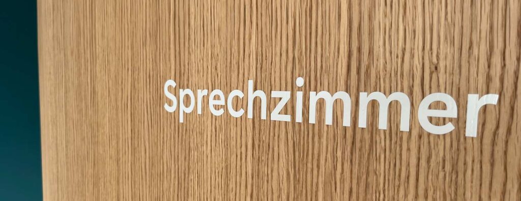 Weisser Schriftzug «Sprechzimmer» auf Holzwand