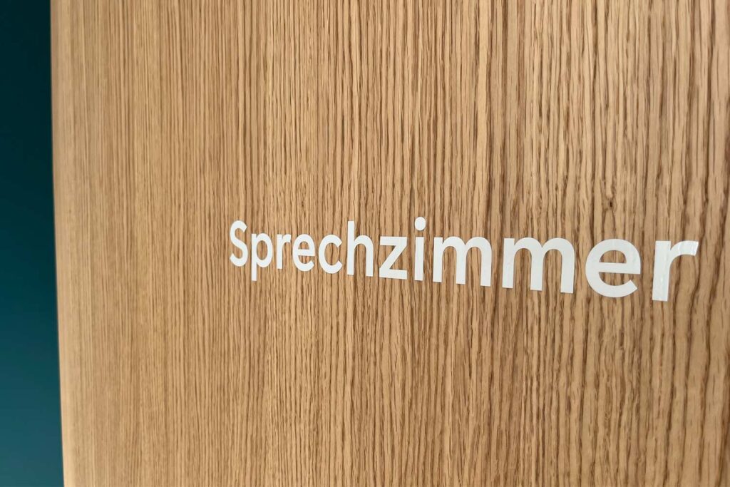 Weisser Schriftzug «Sprechzimmer» auf Holzwand